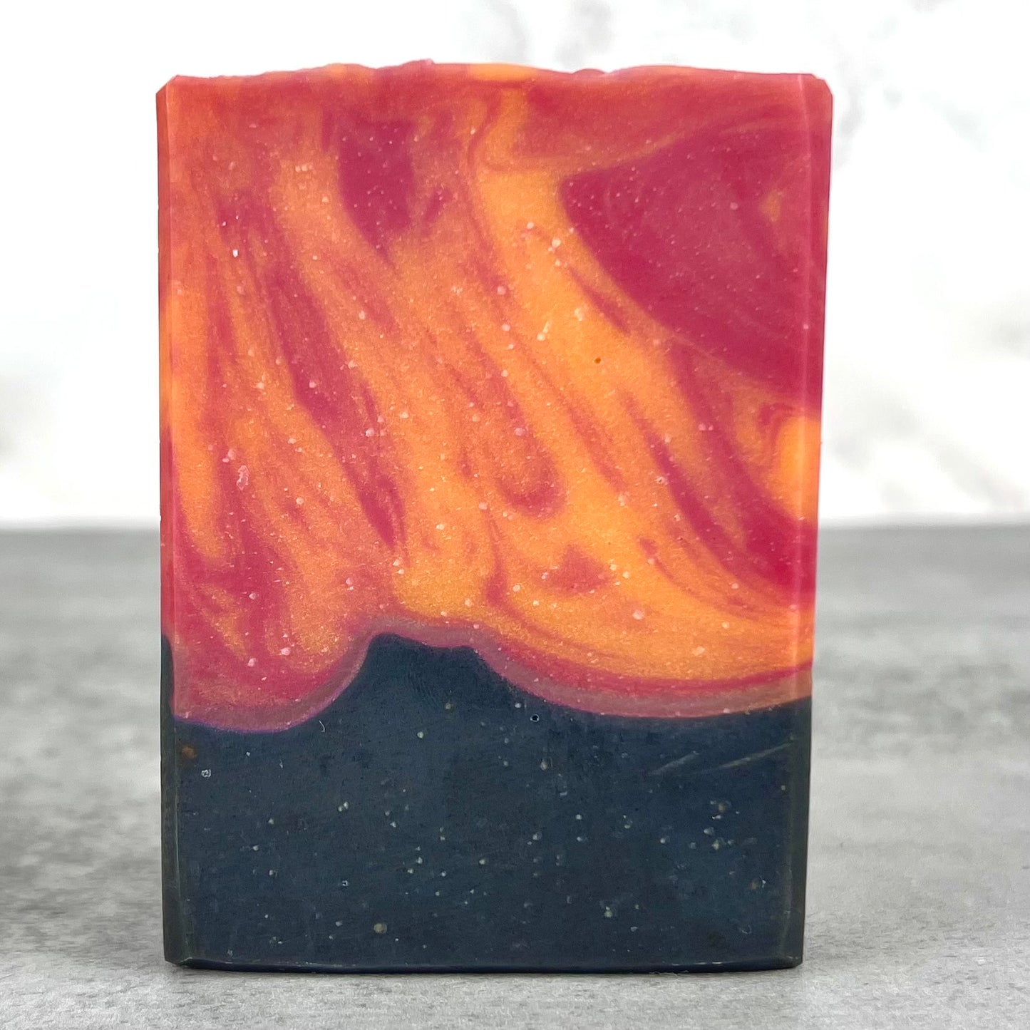 Colorful soap bar with orange, red, and black swirls on a gray surface.