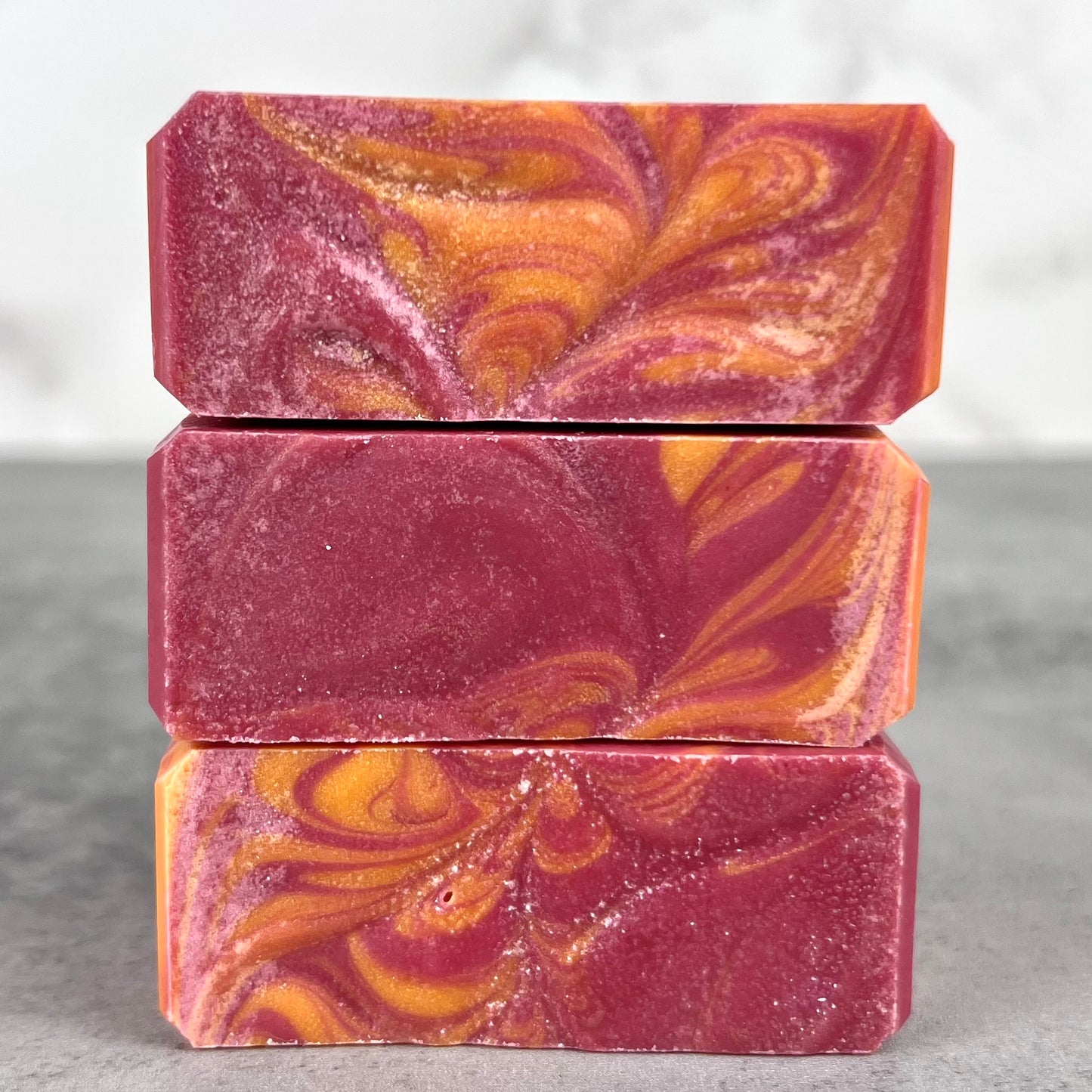 Three bars of marbled soap in pink and orange on a gray surface.