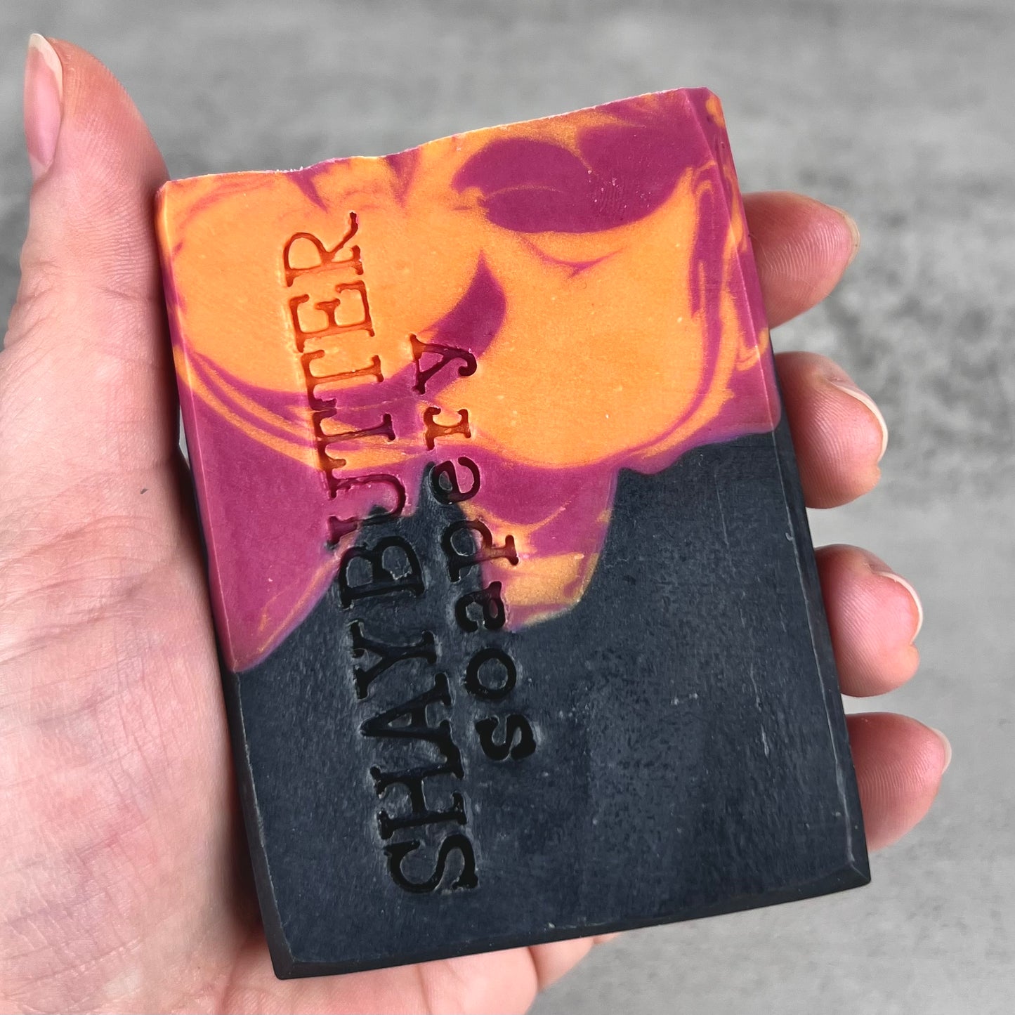 Bar of soap with 'Shay Butter Soapery' branding held in a hand against a gray background