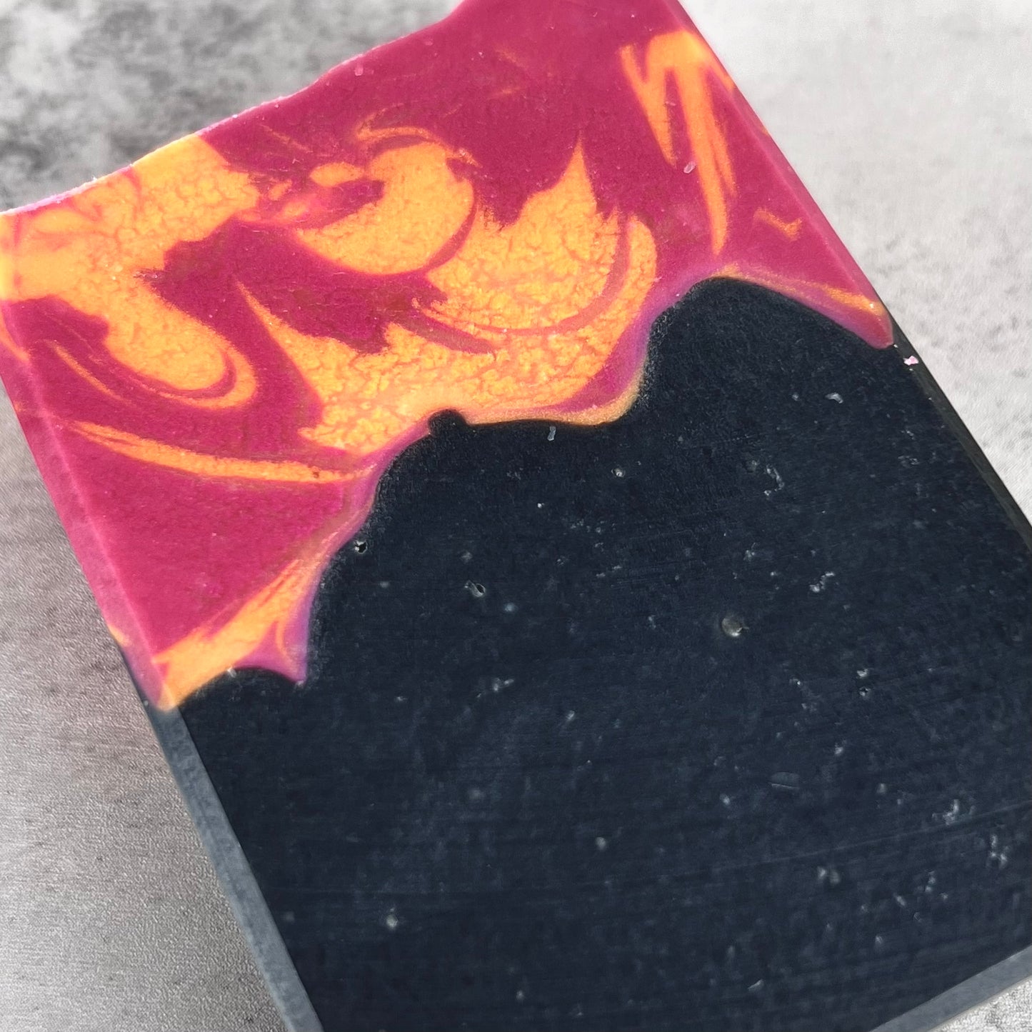Close-up of a marbled soap bar with pink, orange, and black colors on a textured surface.