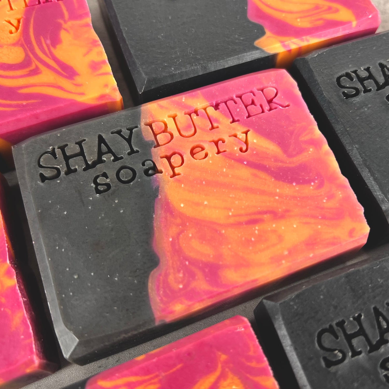 Close-up of Shay Butter Soapery soap bars with colorful swirls and branding.