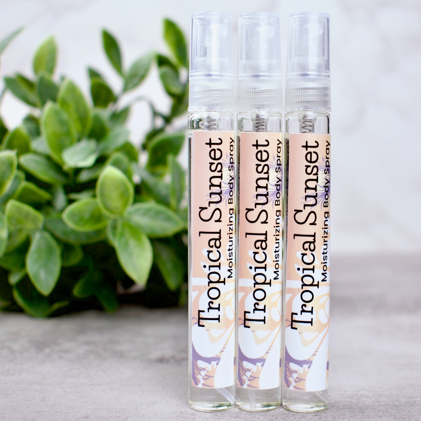 Three bottles of Tropical Sunset moisturizing body spray with a plant in the background.