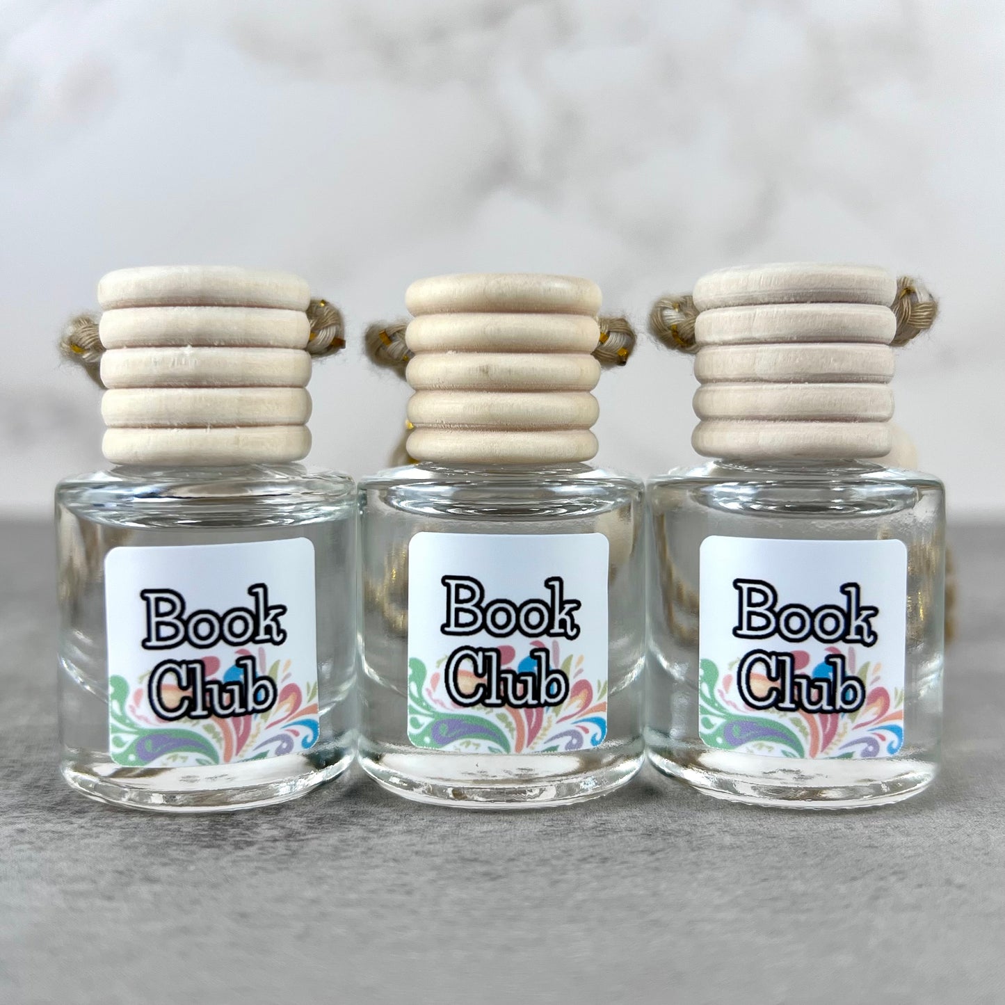 Three car diffusers with wooden lids and 'Book Club' labels on a neutral background