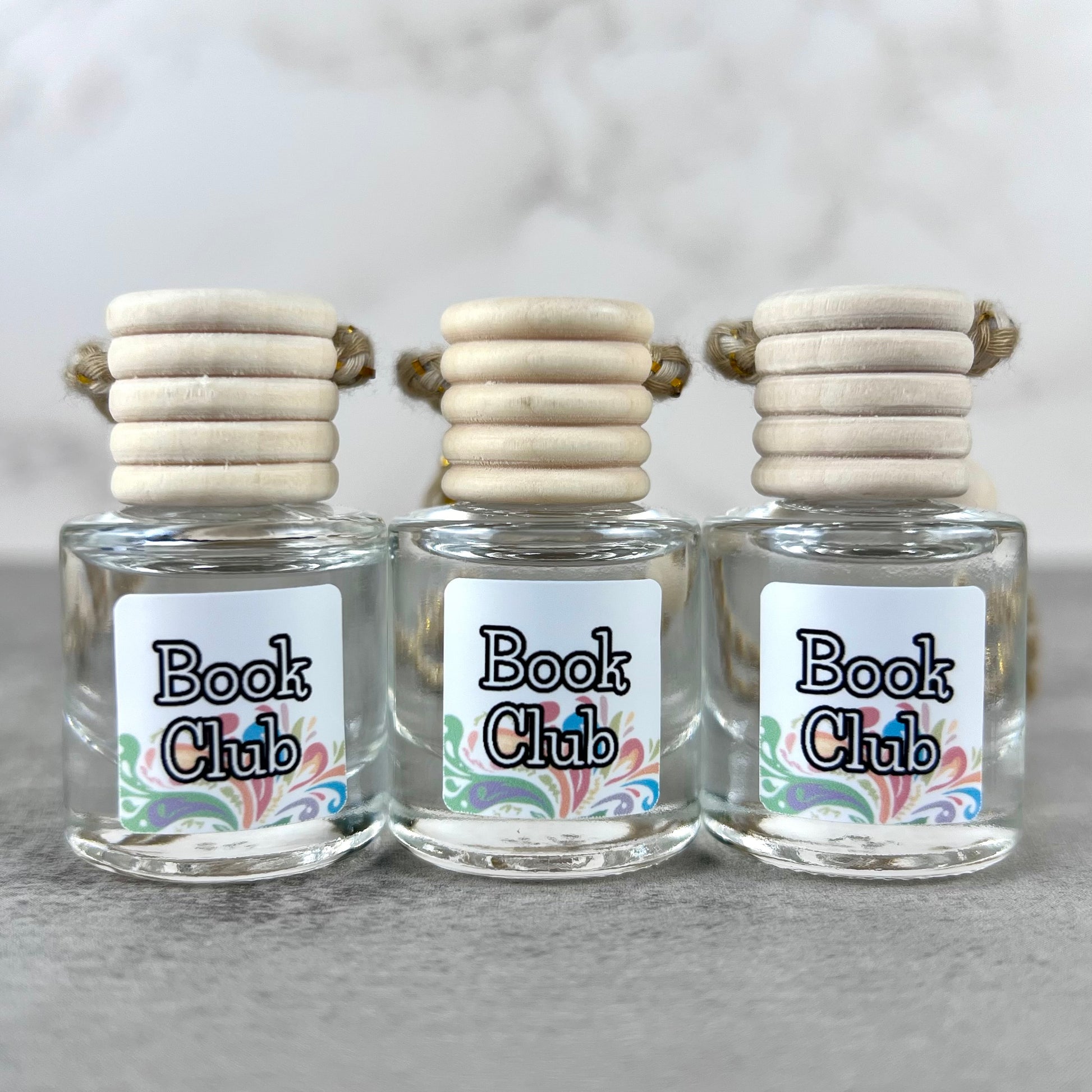 Three car diffusers with wooden lids and 'Book Club' labels on a neutral background