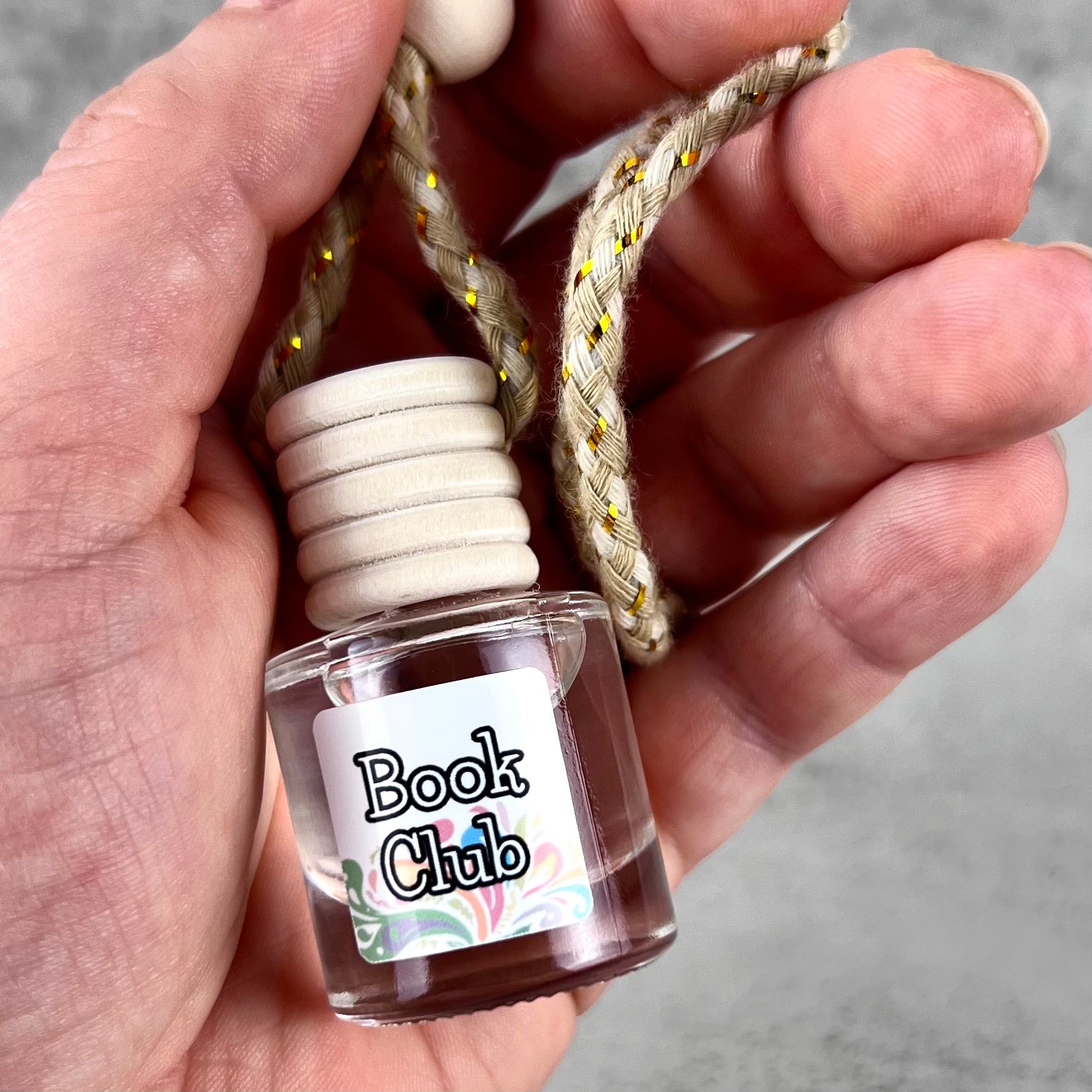 Car diffuser with a wooden cap held in a hand, labeled 'Book Club' on a gray background.