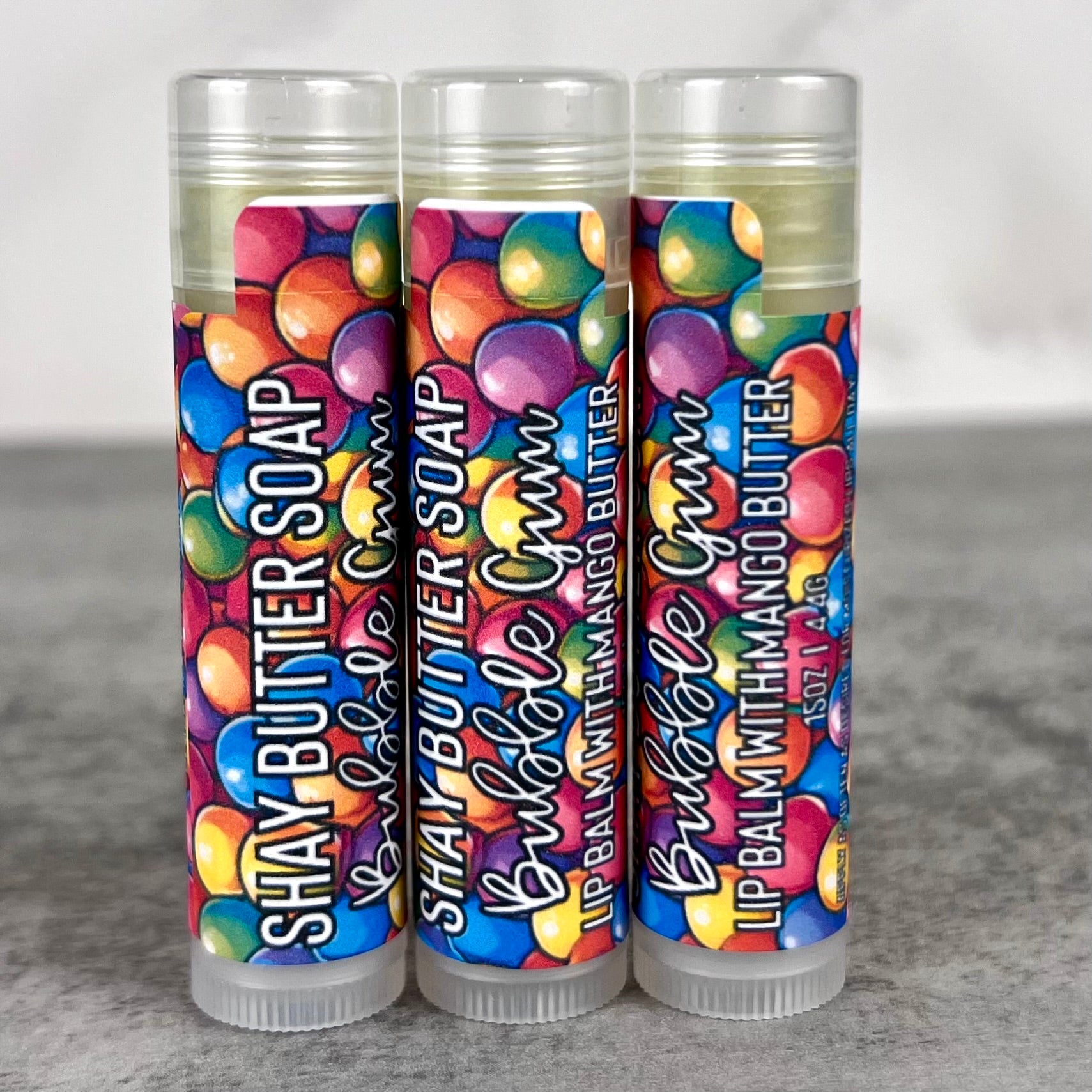 Three lip balm tubes with colorful packaging on a gray surface