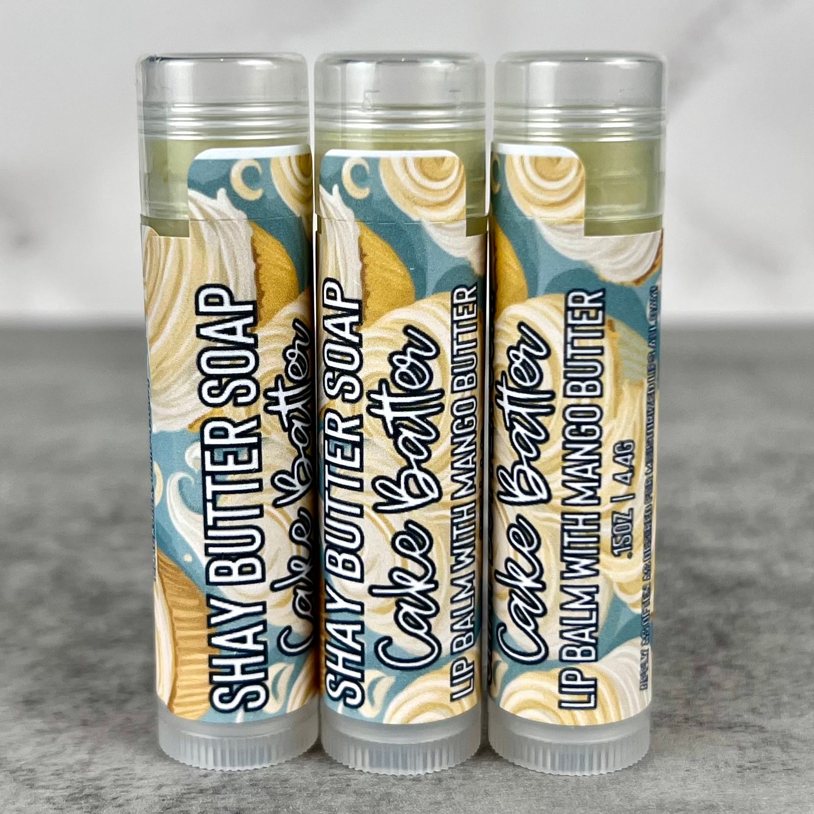 Three tubes of Cake Batter lip balm on a gray surface.