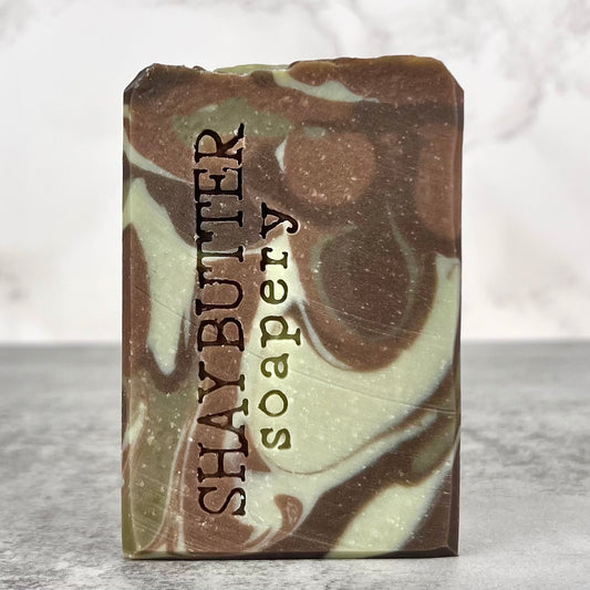 Marbled brown and green soap bar with 'Shay Butter Soapery' branding on a gray surface.