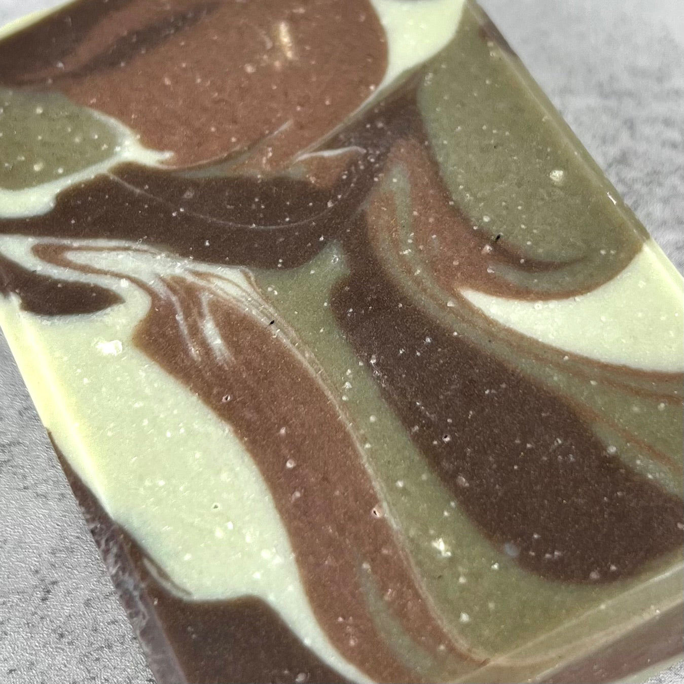 Swirled bar of soap with brown and green colors on a gray background