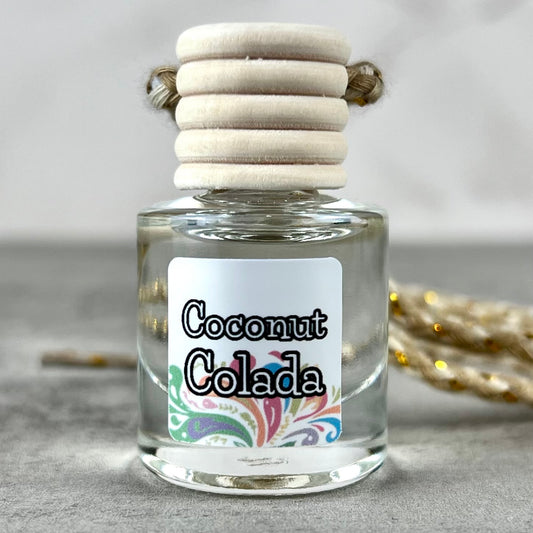 Car diffuser labeled 'Coconut Colada' with a wooden cap on a neutral background