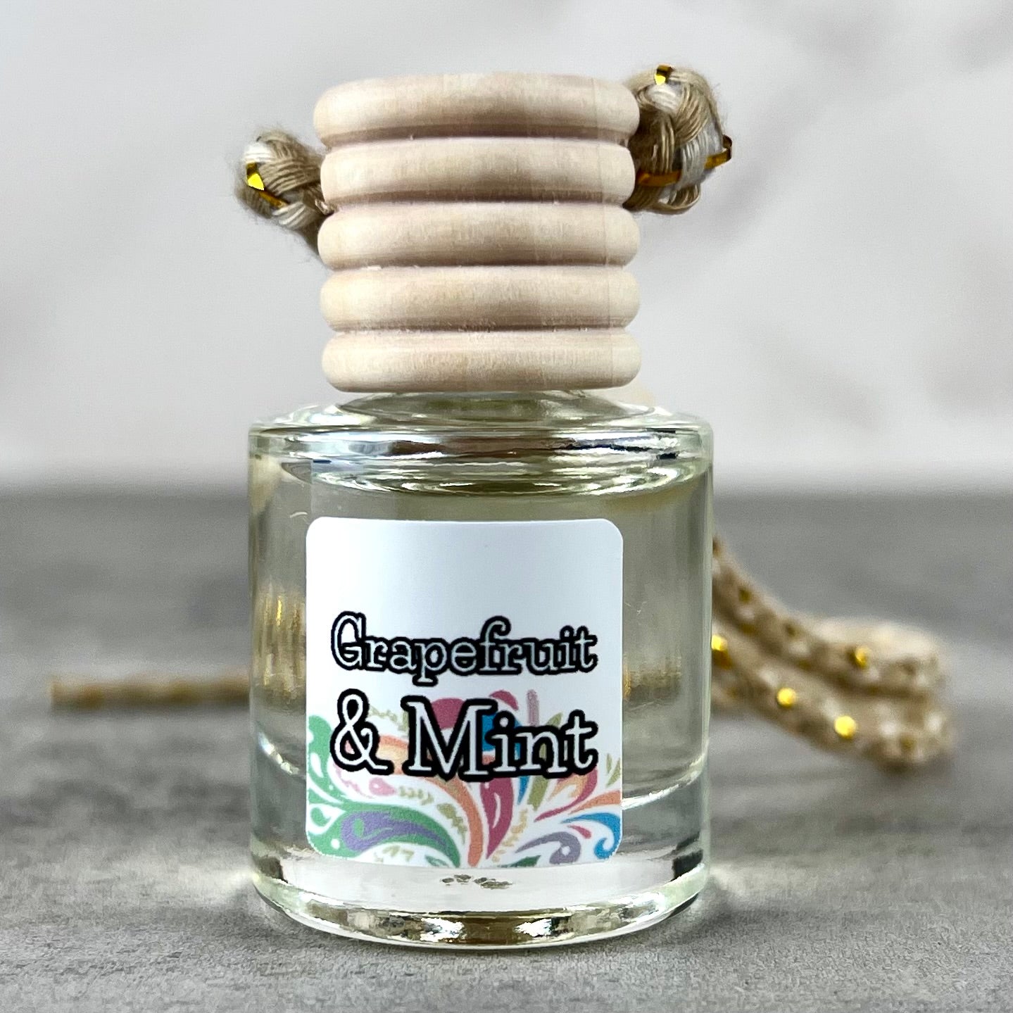 Hanging car diffuser labeled 'Grapefruit & Mint' on a neutral background