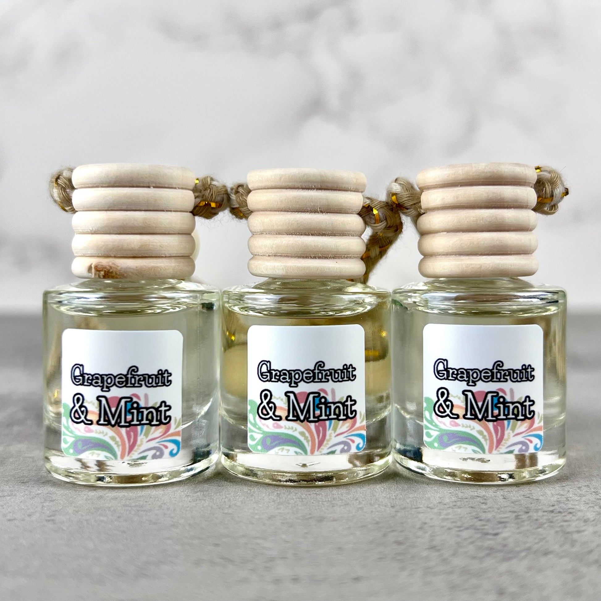 Three hanging car diffusers labeled 'Grapefruit & Mint' with wooden caps on a gray background.