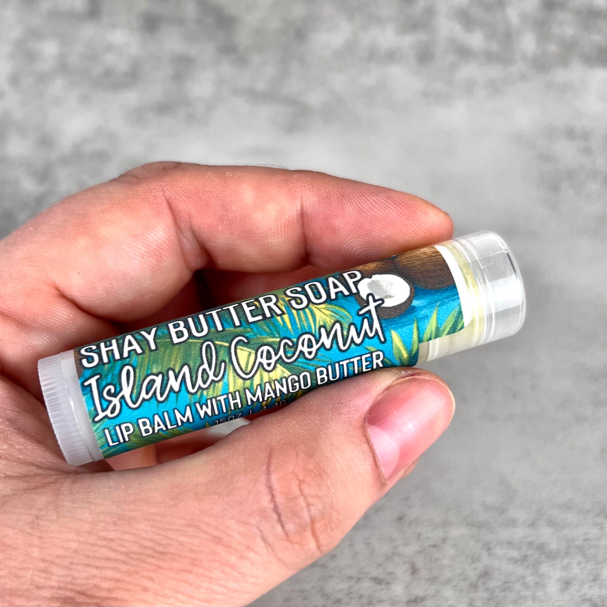 Lip balm with 'Shay Butter Soap' label held in a hand against a gray background
