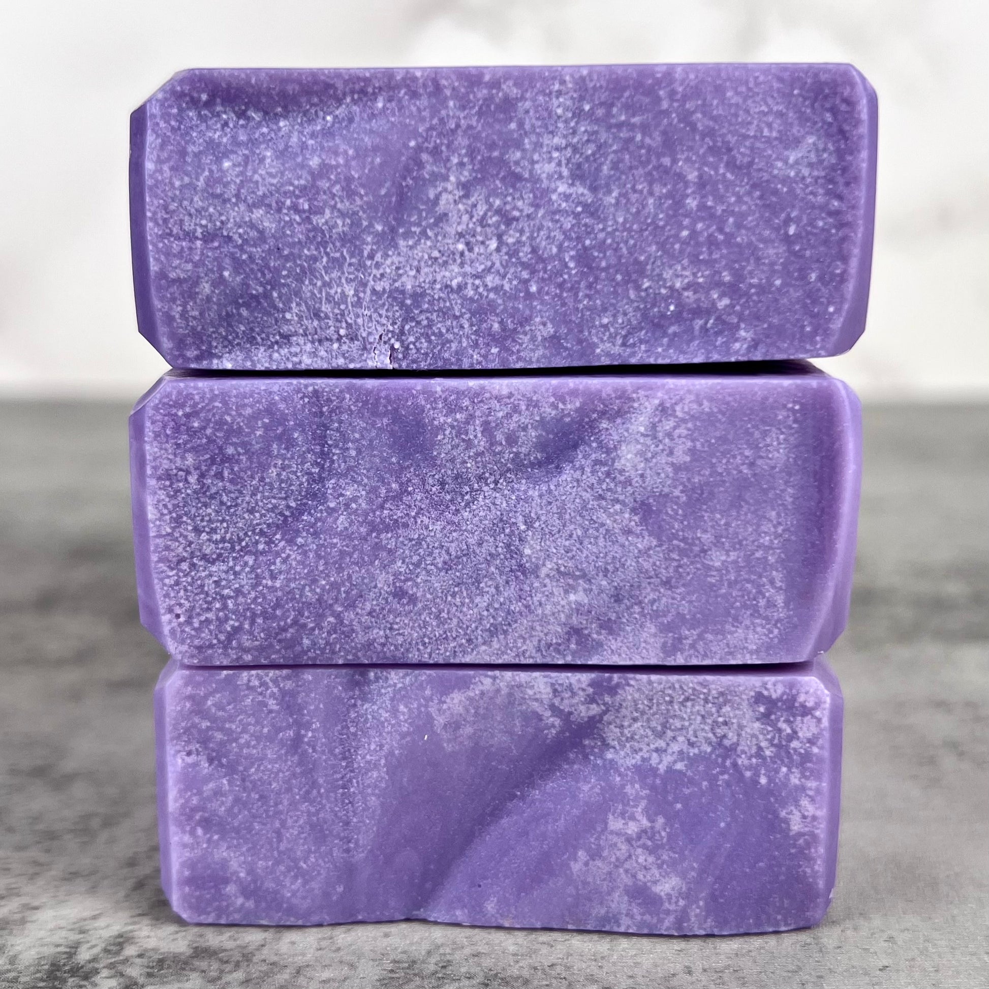 Three stacked purple soap bars on a gray surface with a neutral background