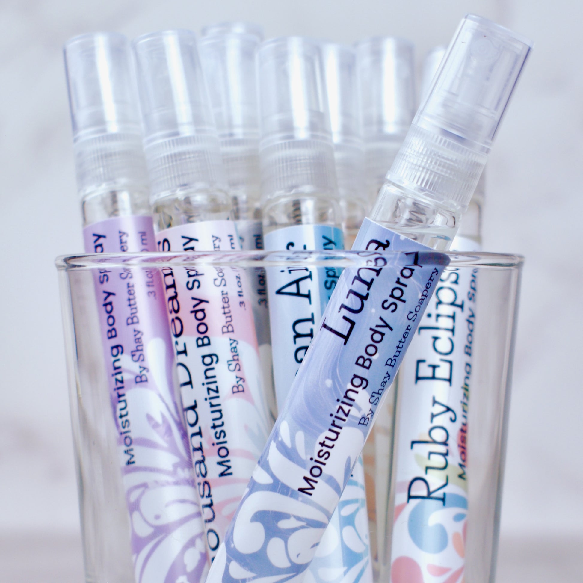 Clear spray bottles with colorful labels in a glass container on a light background