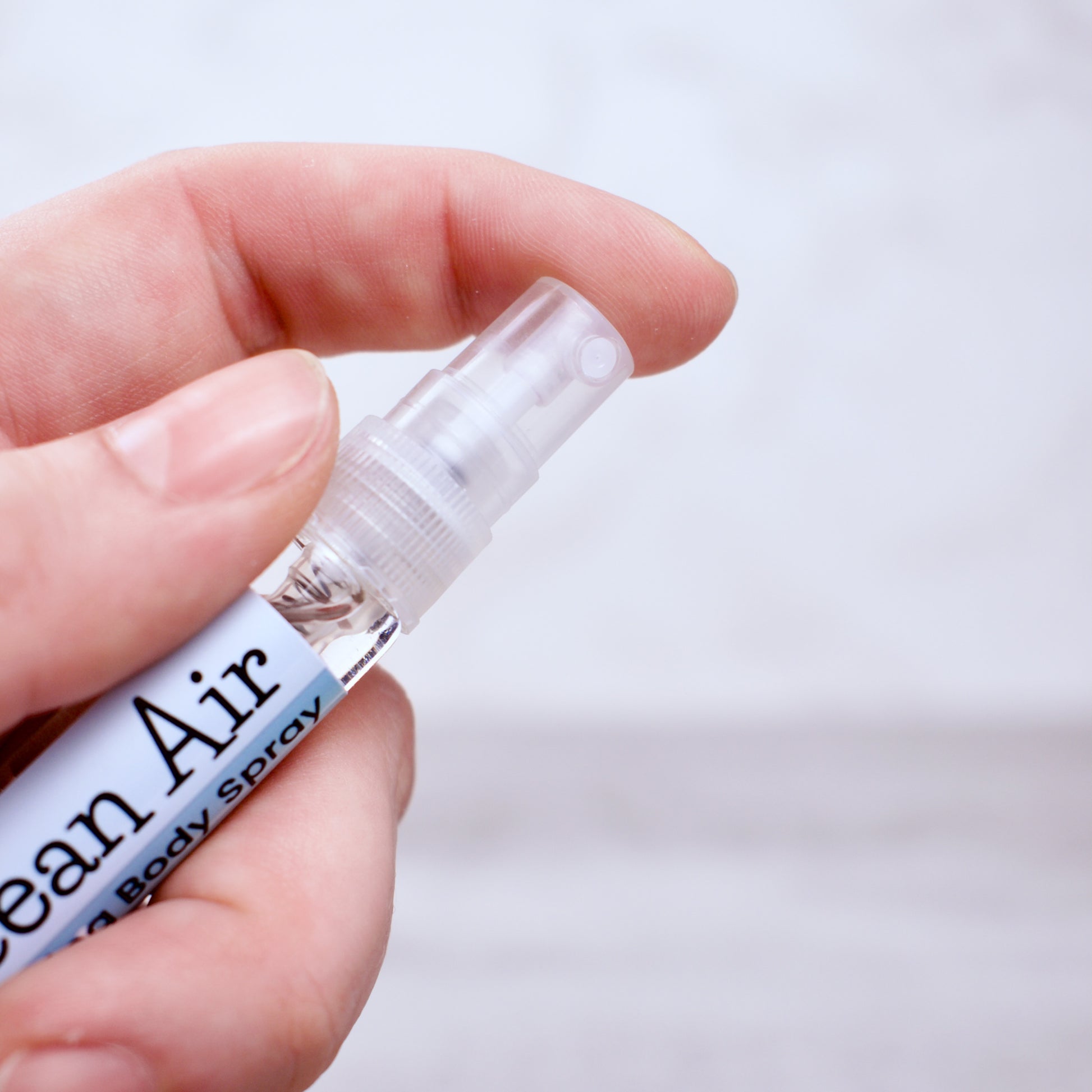 Hand holding a small spray bottle labeled 'Ocean Air' against a light background