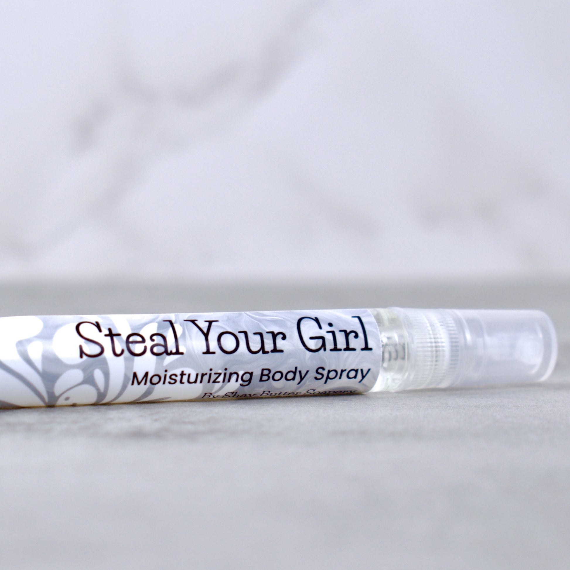 Moisturizing body spray labeled 'Steal Your Girl' on a marble surface with a light gray background