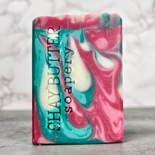 Marbled pink and blue soap bar with 'Shay Butter Soapery' branding on a gray background