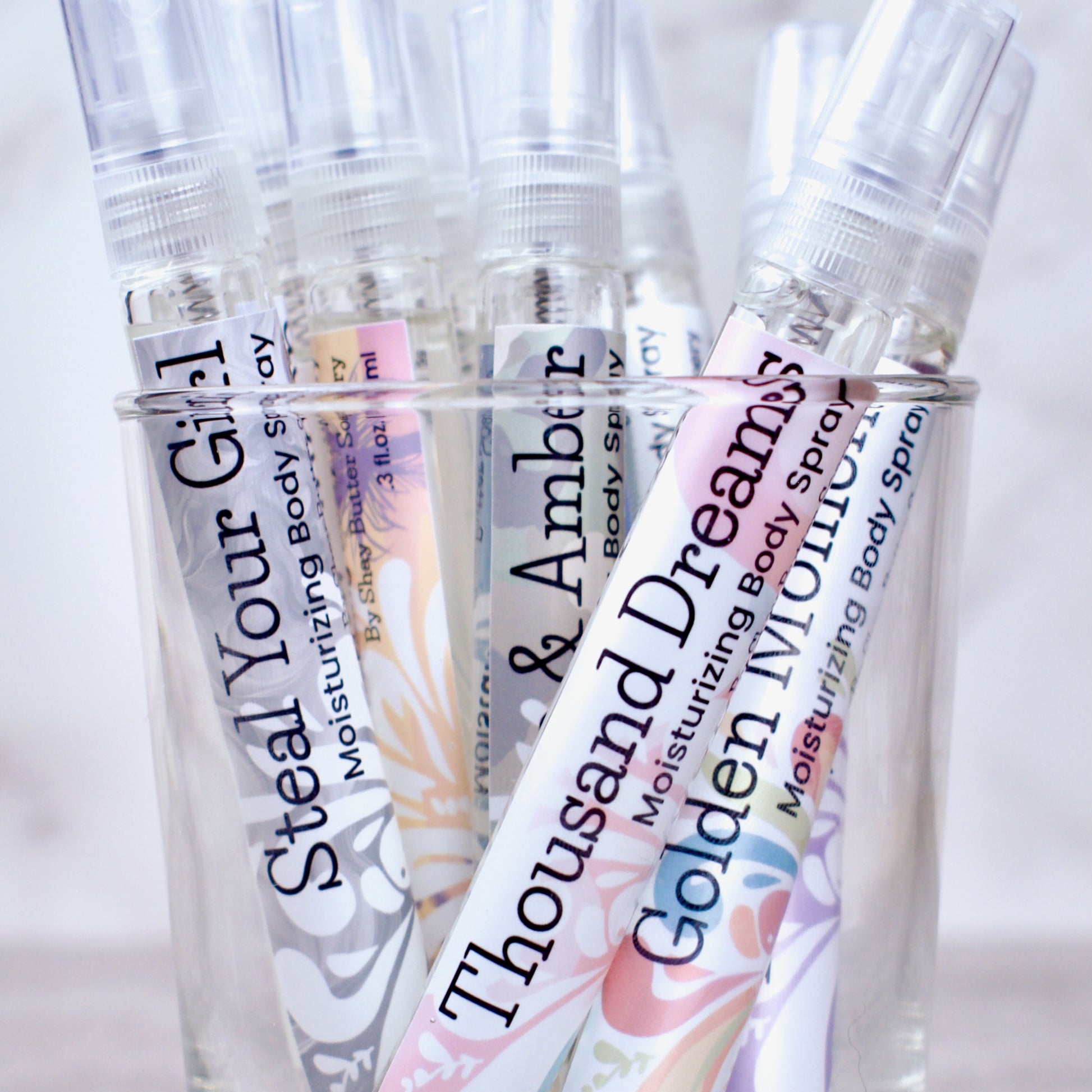 Collection of moisturizing body spray bottles with colorful labels on a light background