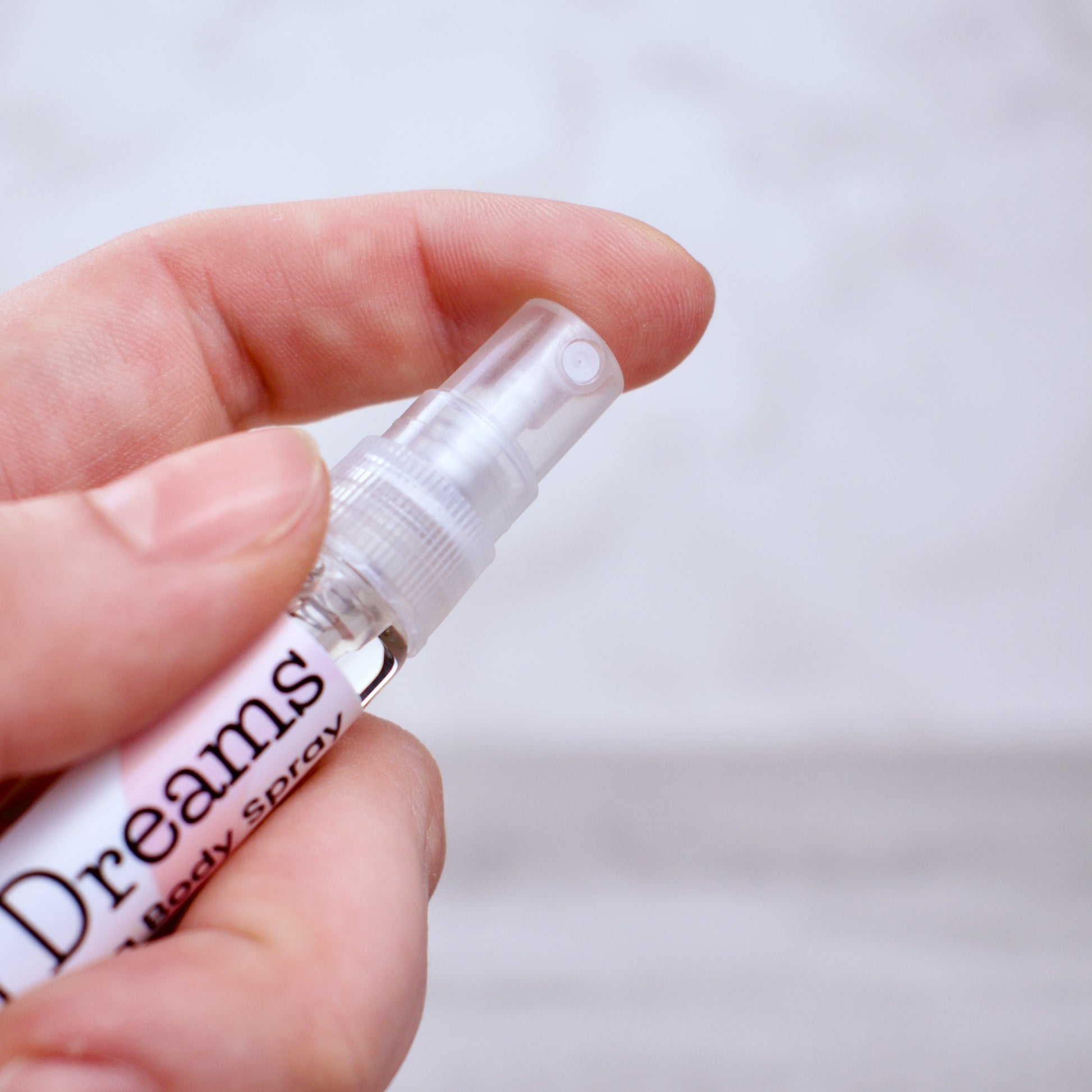 Hand holding a small spray bottle labeled 'Thousand Dreams' against a light background