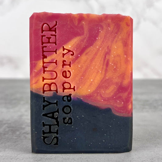 Bar of soap with marbled design and 'Shay Butter Soapery' branding on a neutral background