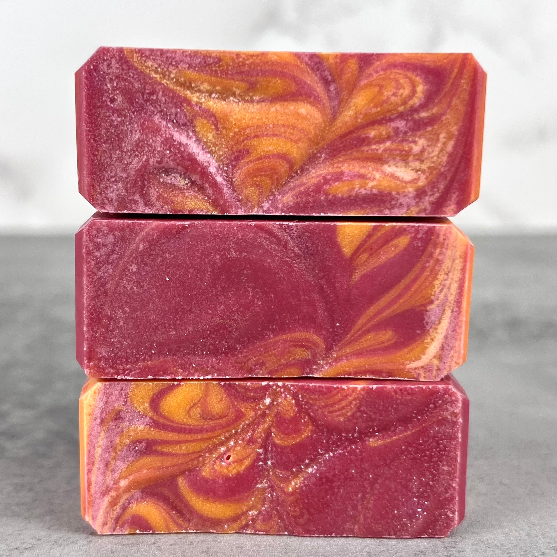 Three bars of marbled soap in pink and orange on a gray surface.